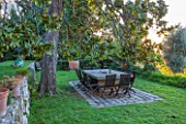 CLOS DU PEYRONNET, MENTON, FRANCE: A PLACE TO SIT: STONE TABLE WITH WOODEN CHAIRS BENEATH A MAGNOLIA TREE. ENTERTAINING, DINING, TERRACE, MEDITERRANEAN