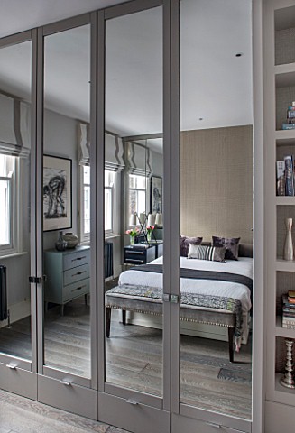 SALLY_STOREY_HOUSE_LONDON_MASTER_BEDROOM_WITH_BED_CUSHIONS_AND_SIDEBOARDS_REFLECTED_IN_THE_MIRRORED_