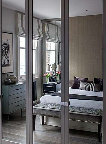 SALLY_STOREY_HOUSE_LONDON_MASTER_BEDROOM_WITH_BED_CUSHIONS_AND_SIDEBOARDS_REFLECTED_IN_THE_MIRRORED_