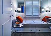 SALLY STOREY HOUSE, LONDON: BEDROOM IN WHITE AND ORANGE WITH ORANGE CUSHIONS AND STORAGE UNITS BENEATH MATTRESS - SHUTTERS, LIGHT, LIGHTS, LIGHTING