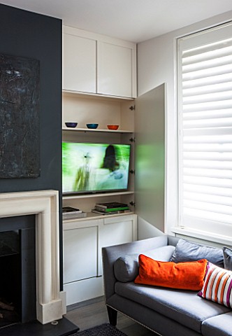 SALLY_STOREY_HOUSE_LONDON_WHITE_PAINTED_WOODEN_WALL_PANELS_IN_LIVING_ROOM_HALF_OPEN_SHOWING_TV_BEHIN