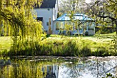 ULTING WICK, ESSEX: VIEW ACROSS LAWN TO THE HOUSE WITH RIVER IN SPRING. APRIL