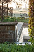 BROUGHTON GRANGE, OXFORDSHIRE: DESIGNER TOM STUART-SMITH - POOL AND WATERFALL IN THE WALLED GARDEN WITH WOODEN BENCH BEHIND - SPRING, WATER, STEPPING STONES, RILL, CANAL