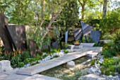 CHELSEA FLOWER SHOW 2016: TELEGRAPH GAREDEN DESIGNED BY ANDY STURGEON - LIMESTONE BRIDGE AND BRONZE FINS BESIDE WATER. LIMESTONE SEATS AND FIREPIT - SEATING, BENCH, BENCHES, PATH