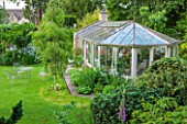 THE LODGE, BURFORD, OXFORDSHIRE: THE PELARGONIUM FILLED CONSERVATORY WITH BETULA PENDULA ON LAWN AND EVERGREENS IN F/G. WITH WHITE FLOWERED SWEET ROCKET AND METAL TABLE & CHAIRS