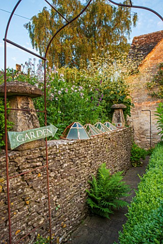 GREYHOUNDS_BURFORD_OXFORDSHIRE_RUSTED_METAL_ARBOUR_WITH_ANTIQUE_CLOCHES_ON_DRY_STONE_WALL_AND_BORDER
