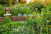 GREYHOUNDS, BURFORD, OXFORDSHIRE: DRY STONE WALL WITH OLD GLASS CLOCHES AND BORDER BEHOND WITH HESPERIS. COTTAGE STYLE PLANTING, INFORMAL