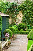 RADFORDS, BURFORD, OXFORDSHIRE: PAINTED GARDEN SHED WITH STONE PATH AND BENCH. BOX TOPIARY SHAPES AND PINK CLIMBING ROSE - ROSA MME ALFRED CARRIERE ON WALL