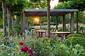PRIVATE GARDEN, GLOUCESTERSHIRE DESIGNED BY MARCUS BARNETT: COUNTRY, GARDEN, SUMMER, ENTERTAINING, COTSWOLDS, WOODEN PERGOLA, TABLE, CHAIRS, SEATING, SUNSET