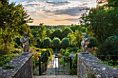 EASTLEACH HOUSE, GLOUCESTERSHIRE: VIEW THROUGH GATES DOWN THE RILL TO SORBUS ARIA LUTESCENS. STATUES, STONE, WALL, SKY, EVENING LIGHT, COUNTRY GARDEN