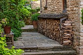 CALENDARS: BURFORD,OXFORDSHIRE:STONE STEPS UP TO LOG STORE/PILE OPPOSITE WALL WITH FIG TREE, CHOISYA & POT OF WHITE AGAPANTHUS.