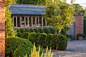 MORTON HALL GARDENS, WORCESTERSHIRE: WEST GARDEN TERRACE, SUNSET, EVENING LIGHT, BUILDING, WINDOWS, CLIPPED BOX HEDGING. HEDGE