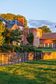 MORTON HALL GARDENS, WORCESTERSHIRE: WEST GARDEN TERRACE, SUNSET, EVENING LIGHT, BUILDING, WINDOWS, CLIPPED BOX HEDGING. HEDGE, WALL, LAWN, SKY