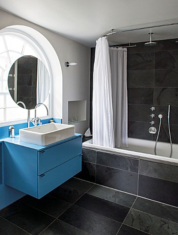 MORTON_HALL_WORCESTERSHIRE_BATHROOM_WITH_ARCHED_WINDOW_FREE_STANDING_CIRCULAR_MIRROR_WITH_BLUE_PAINT