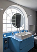 MORTON HALL, WORCESTERSHIRE: BATHROOM WITH ARCHED WINDOW, FREE STANDING CIRCULAR MIRROR AND BLUE PAINTED CABINETS