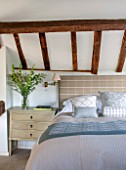 THE COACH HOUSE,SURREY: BEDROOM WITH OAK BEAMS ABOVE BED. SIDE TABLE BY OKA, CUSHIONS AND BED COVER BY HUDSON HOMES & INTERIORS. NEUTRAL DECOR.