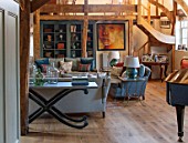 THE COACH HOUSE,SURREY:FAMILY ROOM WITH WOODEN STAIRCASE.SOFAS,CONSOLE TABLE BY ANDREW MARTIN,WOODEN FLOOR, PORTRAIT BY CAROL PEACE,PIANO,BOOKCASE PAINTED IN SQUID INK,LAMPS BY OKA