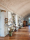 BURTON AGNES HALL, EAST YORKSHIRE: CHRISTMAS - THE LONG GALLERY - WALNUT TREE BOUGHS IN METAL PLANTERS DRAPED IN TINSEL AND SNOWFLAKES. RECONSTRUCTED PLASTERWORK BARREL CEILING