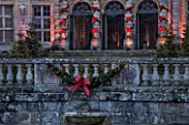 VAUX LE VICOMTE, FRANCE: THE ENTRANCE TO THE PALACE AND MOAT BALLUSTRADE AT CHRISTMAS DECORATED WITH RIBBON BOWS AND CHRISTMAS TREES. TREE, LIGHT, LIGHTING, ILLUMINATION, WINTER