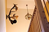 THE FREETH, HEREFORDSHIRE: HALLWAY - PRINT ROOM YELLOW FROM FARROW AND BALL PAINTED WALLS, STAIRS, STAIRCASE, ANTLER HAT RACK, GILT AND GLASS ORB LANTERN