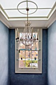 LONDON HOUSE DESIGNED BY JULIE SIMONSEN. CHANDELIER IN STAIRWELL WITH SHELVED WINDOW DISPLAYING GLASS ORNAMENTS.