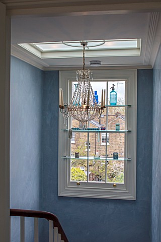 LONDON_HOUSE_DESIGNED_BY_JULIE_SIMONSEN_CHANDELIER_IN_STAIRWELL_WITH_SHELVED_WINDOW_DISPLAYING_GLASS