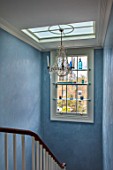 LONDON HOUSE DESIGNED BY JULIE SIMONSEN. CHANDELIER IN STAIRWELL WITH SHELVED WINDOW DISPLAYING GLASS ORNAMENTS.