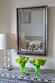 BUTTER WAKEFIELD HOUSE, LONDON: ZOES BEDROOM: MOTHER OF PEARL INLAY CHEST OF DRAWERS WITH ANTIQUE BLACK & WHITE MIRROR AND GLASS LAMP. GREEN GLASS CONTAINERS WITH VIBURNUM