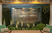 DAVID HARBER SUNDIALS: CHELSEA 2017. BRONZE WAVE WATER WALL WITH WHITE FOXGLOVES AND SEATING AREA. WATER FEATURE, SEAT, RELAX, CONTEMPORARY, LIGHTING, LIT, LIGHT, EVENING, ENTERTAI