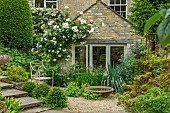 THE LODGE, OXFORDSHIRE:DESIGNER SUSAN ASHTON.SHALLOW BIRD BATH OUTSIDE KITCHEN WITH IRIS SIBIRICA AND YUCCA GLORIOSA. HOUSE, COUNTRY COTTAGE, GARDEN, STEPS, OLD METAL CHAIR, RUSTIC