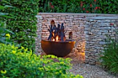 THE OLD RECTORY, QUINTON, NORTHAMPTONSHIRE: DESIGNER ANOUSHKA FEILER: FIRE GARDEN. METAL FIRE PIT, SCULPTURE BY CATHY AZRIA. LIGHTING, LIT UP, NIGHT. WALL, ORNAMENT, DRY, STONE