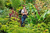 SWEETBRIAR, KENT: STEVE EDNEY, LOUISE DOWLE IN GARDEN WITH BIG LEAVES AND FOLIAGE OF PLANTS. GREEN, PEOPLE, GARDEN, SUMMER, ALBIZIA JULIBRISSIN ROSEA, MUSA SIKKIMENSIS, AMARANTHUS