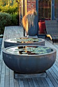 PRIVATE GARDEN, SURREY: DESIGNER ANTHONY PAUL: DECKED GARDEN, CONTAINERS, WATERLILIES. DECKING, ROUND, CIRCULAR, SUNSET, EVENING, LIGHT, FORMAL, SMALL, ENGLISH, COUNTRY
