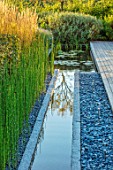 PRIVATE GARDEN, SURREY: DESIGNER ANTHONY PAUL: GRANITE RILL, POND, POOL, WATER, PEBBLES, FEATURE, REEDS, EQUISETUM, HYEMALE, HORSETAIL, GREEN, FOLIAGE, GRASS, PERENNIALS, DECKING