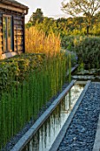 PRIVATE GARDEN, SURREY: DESIGNER ANTHONY PAUL: GRANITE RILL, POND, POOL, WATER, PEBBLES, FEATURE, REEDS, EQUISETUM, HYEMALE, HORSETAIL, GREEN, FOLIAGE, GRASS, PERENNIALS, DECKING
