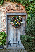 BADDESLEY CLINTON, WARWICKSHIRE: THE NATIONAL TRUST- CHRISTMAS, 15TH AND 16TH CENTURY MOATED MANOR HOUSE. WOODEN DOOR, HOME GROWN, HOMEMADE DRIED FLOWER WREATH