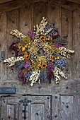 BADDESLEY CLINTON, WARWICKSHIRE: THE NATIONAL TRUST- CHRISTMAS, 15TH AND 16TH CENTURY MOATED MANOR HOUSE. GATEHOUSE WOODEN DOOR, HOME GROWN, HOMEMADE DRIED FLOWER WREATH