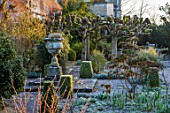 RODMARTON MANOR, GLOUCESTERSHIRE, WINTER, STONE URN IN CENTRE OF LEISURE GARDEN WITH MANOR BEHIND. ENGLISH, COUNTRY, GARDEN, FEBRUARY
