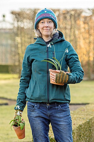 THENFORD_GARDENS__ARBORETUM_NORTHAMPTONSHIRE_GADENER_EMMA_THICK_HOLDING_TERRACOTTA_CONTAINERS_OF_SNO