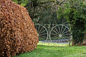 OLD COUNTRY FARM, WORCESTERSHIRE: BEECH HEDGE AND ORNATE METAL GATE BESIDE GRASS PATH. ENGLISH, COUNTRY, GARDEN, BOUNDARIES, MARCH