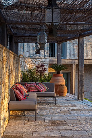 SKOPOS_DESIGN_CORFU_STONE_TERRACE_WITH_SEATING_CUSHIONS_TERRACOTTA_CONTAINERS_PERGOLA_COVERED_NEDITE