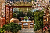 ASCOT SPRING GARDEN SHOW: GARDEN DESIGNED BY KATE GOULD: TABLE, CHAIRS, TERRACOTTA CONTAINER, CORTEN STEEL PERGOLA, SCREENS, SCREENING, DINING, FORMAL, URBAN, SMALL, CHERRY, PRUNUS