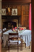 WARDINGTON MANOR, OXFORDSHIRE: DINING ROOM, LINEN TABLECLOTH, TULIPS IN GLASS VASES, CANDLES, DARK WOOD PANELLING