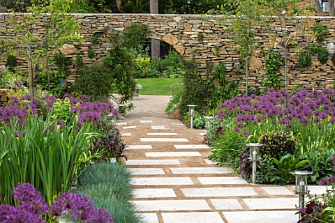 THE_MOONGATE_GARDEN_SUSSEX_PATH_BORDERS_IN_SPRING_OF_ALLIUM_FIRMAMENT_WITH_PURBECK_STONE_WALL_MOONGA
