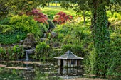 CHILWORTH MANOR, SURREY: ORIGINAL MONASTIC STEWPOND WITH WATERFALL AND JAPANESE MAPLES IN SPRING, DUCK HOUSE