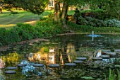 CHILWORTH MANOR, SURREY: STEPPING STONES OVER ORIGINAL MONASTIC STEWPOND WITH FOUNTAIN AND HOUSE REFLECTED IN THE POOL