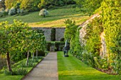 CHILWORTH MANOR, SURREY: THE WALLED GARDEN. GRAVEL PATH PAST LAWN AND SCULPTURE IN SPRING