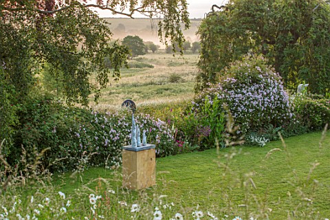 ASTHALL_MANOR_OXFORDSHIRE_LAWN_WITH_ROSES_HEDGE_AND_MEADOW_BEYOND_SCULPTURE_SOGNO_DALTEZZA_BY_ROB_GO