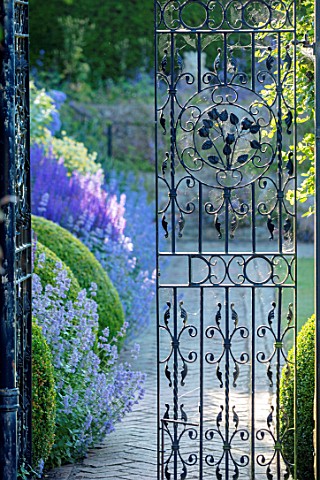 TOWN_PLACE_GARDEN_SUSSEX_VIEW_THROUGH_HALF_OPENED_WROUGHT_IRON_GATE_TO_PATH_HERBACEOUS_BORDER_SUMMER