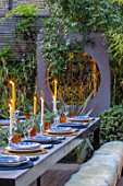 TANYA SOUTHWORTH GARDEN, LONDON, DESIGNER ANOUSHKA FEILER: SMALL GARDEN - TABLE, BENCHES, CANDLES, RENDERED WALL WITH CIRCLE THROUGH IT, LIGHTING, EVENING, NIGHT, FORMAL